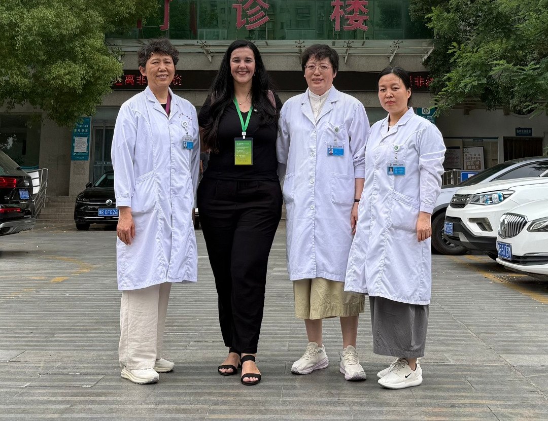 Layla Souza com três profissionais de saúde de jaleco em frente ao Nanyang Second General Hospital, na China