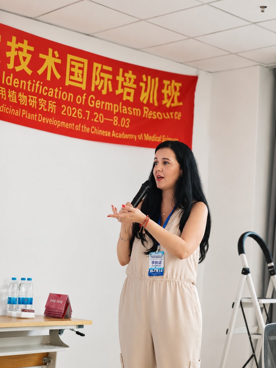 Layla Souza falando ao microfone durante a sua palestra no treinamento internacional na China, diante de uma faixa vermelha em chinês e inglês com o nome do curso e as datas