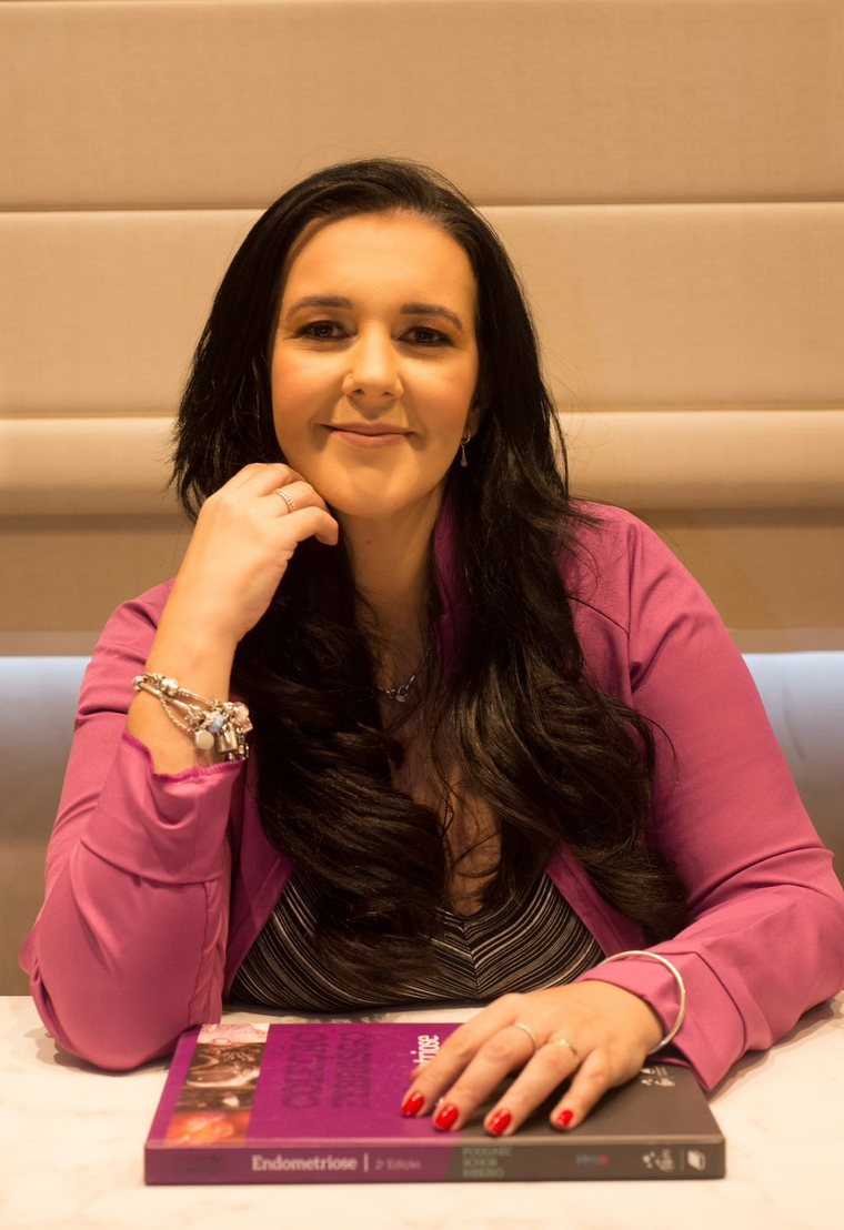 Layla Souza sentada à mesa do consultório, com um livro sobre endometriose à frente